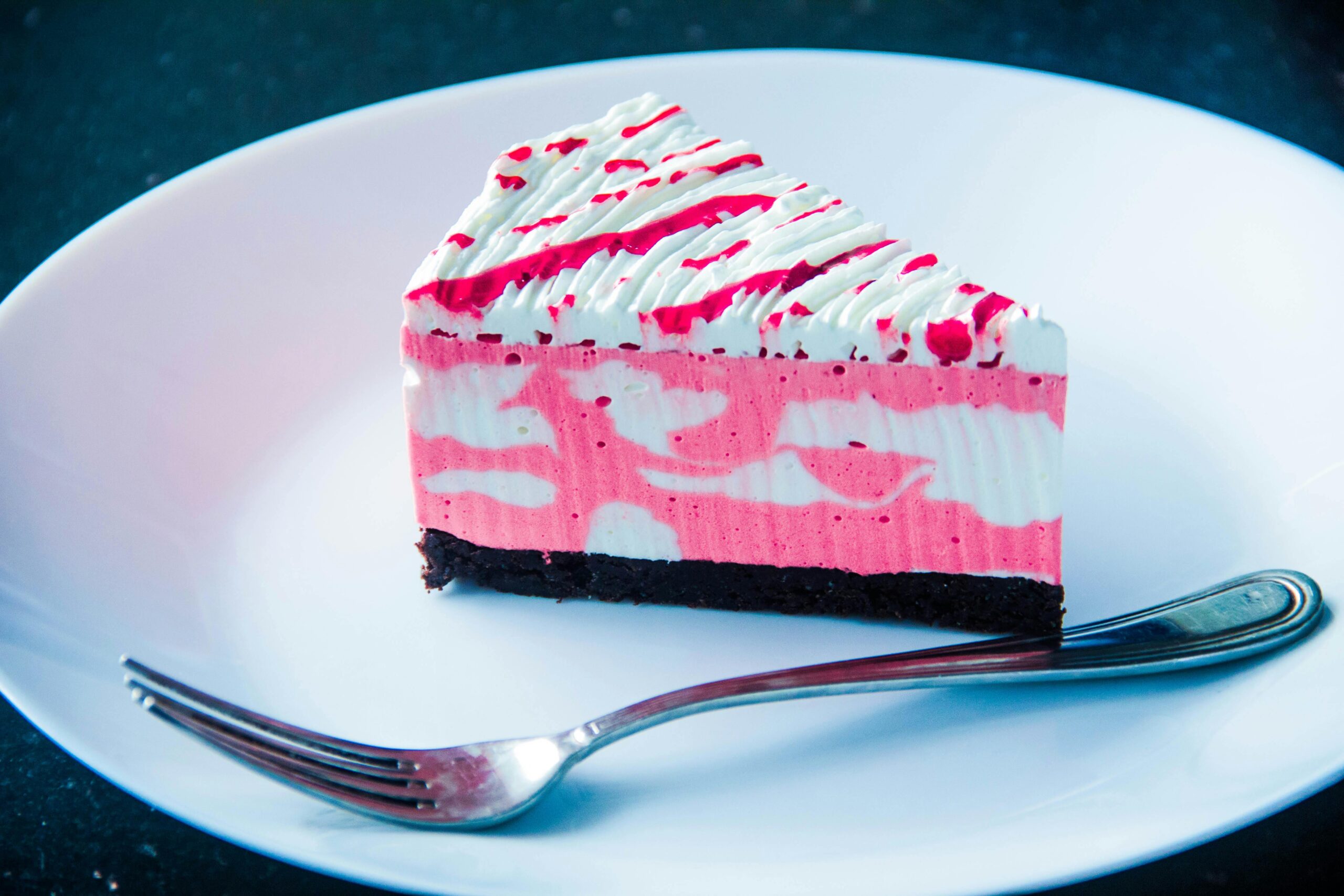 Close-up of a vibrant raspberry cream cake slice with a fork on a plate, perfect for dessert lovers.