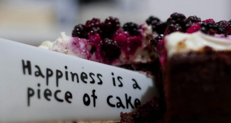 Slice of berry-topped cheesecake with a message plate saying 'Happiness is a piece of cake'.